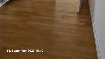 A hallway with wooden flooring, white walls, and two potted plants.