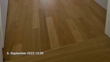 A room with a sloped ceiling, a bed with a striped pillow, a painting on the wall, and a wooden floor.