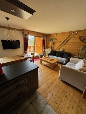 Un salon chaleureux avec un plancher en bois, un canapé, une table basse et un téléviseur fixé au mur.