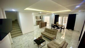 A spacious living area with a sofa set, a coffee table, and a dining table with chairs. A kitchen is visible in the background, and there is a staircase leading to another level. - Espaciosa y Comoda Casa en Frente de la Plazajazz (Santa Cruz de Mompox)