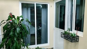A room with a large sliding glass door, a potted plant, and a small shelf with additional plants.