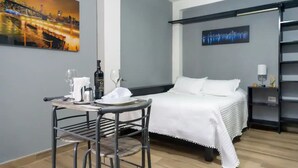 A hotel room with a bed, a table with a bottle and glasses, and a painting on the wall.