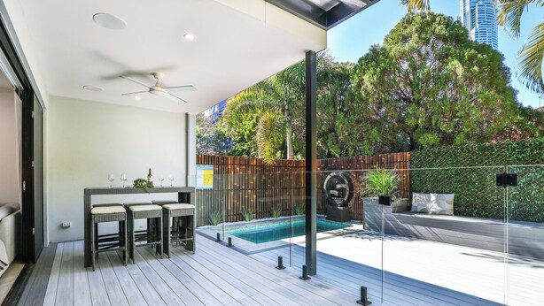 A modern outdoor patio with a pool, seating area, and a view of the surrounding greenery and buildings.