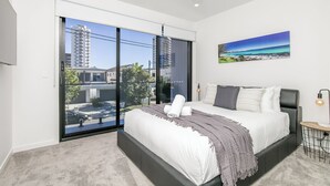 A modern bedroom with a large bed, a view of the city through floor-to-ceiling windows, and a ceiling fan.