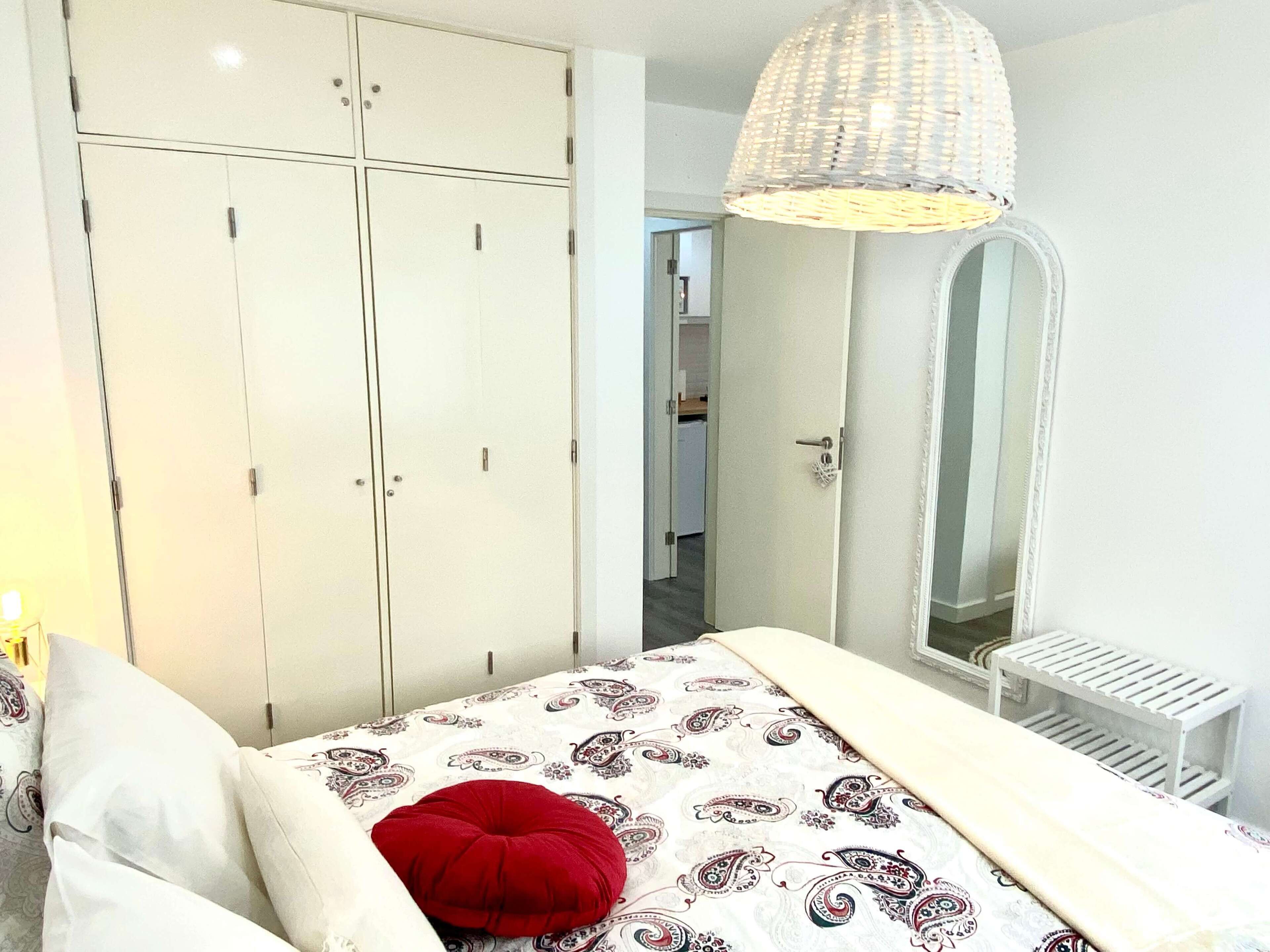 A bedroom with a bed, a wardrobe, a mirror, and a hanging light fixture.