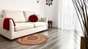 Ein modernes Wohnzimmer mit einem beigefarbenen Sofa, einem roten Kissen, einem gemusterten Teppich und einem kleinen Holztisch.