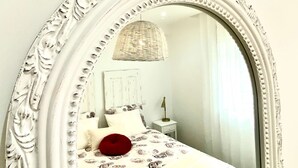 Ein Schlafzimmer mit einem großen, verzierten Spiegel, einem Bett mit gemusterten Bettbezügen, einem roten Kissen, einer Nachttischlampe und einer gewebten Leuchte.