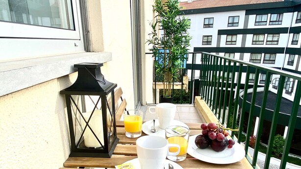 Ein Balkon mit einem Holztisch, gedeckt für das Frühstück, einschließlich einer Kerze, einem Glas Orangensaft, einer Traubenteller und einer Marmeladengläschen.