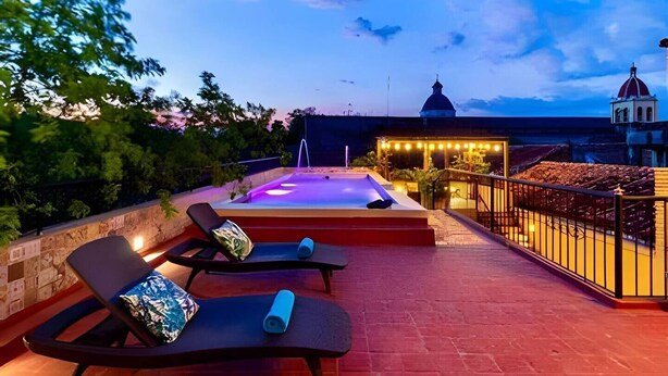 Una terraza en la azotea con bañera de hidromasaje, sillas de descanso y vistas a un edificio histórico.