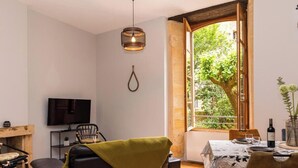 Un salon confortable avec une grande fenêtre, un téléviseur et un coin repas avec une table mise pour deux personnes.