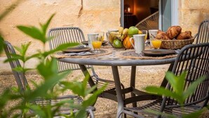 Un espace extérieur aménagé pour prendre les repas, avec un mur en pierre, une table dressée pour le petit-déjeuner et des chaises.