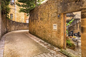 A narrow alleyway with stone walls, a small door, and a table with outdoor seating. - Le jardin de la Paix - Historic centre (Sarlat-la-Canéda)
