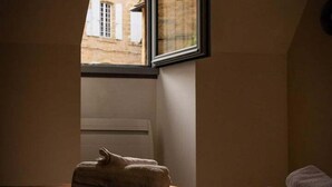 Une chambre avec un plafond en pente, une fenêtre donnant sur un bâtiment à l’extérieur, un lit avec une couverture et un oreiller sur le lit.
