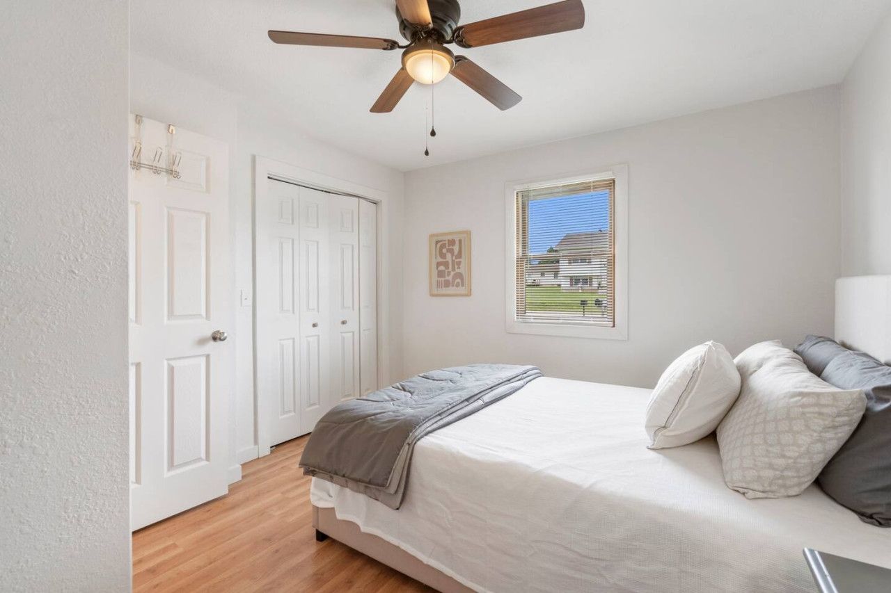 A bedroom with a bed, a ceiling fan, a window with blinds, and a door.