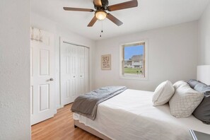 A bedroom with a bed, a ceiling fan, a window with blinds, and a door.