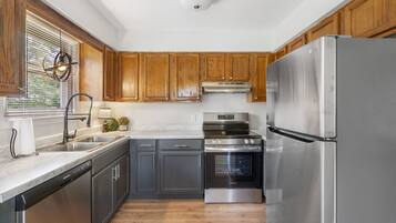 A kitchen with wooden cabinets, stainless steel appliances, a dishwasher, and a window with blinds.
