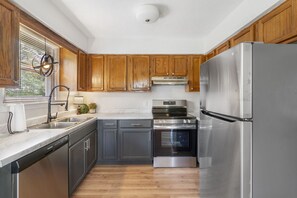 A kitchen with wooden cabinets, stainless steel appliances, a dishwasher, and a window with blinds.