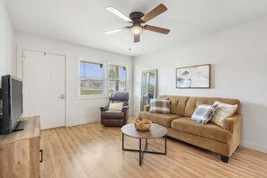 A living room with a ceiling fan, a brown leather chair, a brown sofa with pillows, a small round coffee table, and a television on a wooden stand.