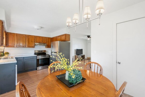 A modern kitchen with wooden cabinets, stainless steel appliances, and a dining area with a round table and chairs.