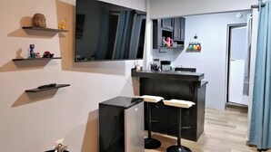Cozinha moderna com televisão de tela plana, área de bar com banquetas e uma pequena estante com objetos decorativos.
