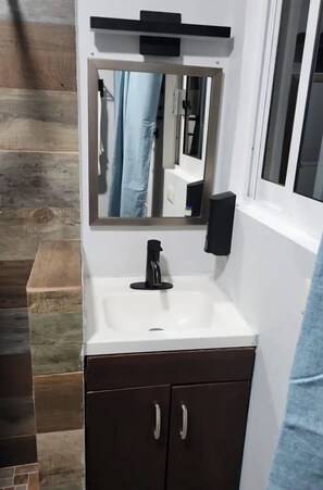 Une salle de bain avec un lavabo blanc, des meubles sombres, un miroir et une fenêtre.