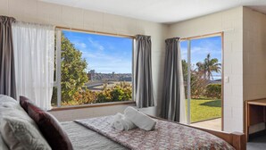 A hotel room with a large bed, a view of a cityscape and greenery, and a sliding glass door to the outside.