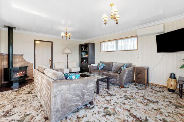 A living room with a fireplace, sofas, a coffee table, and a TV. - Bay View Gardens - Tauranga Holiday Home (Tauranga)