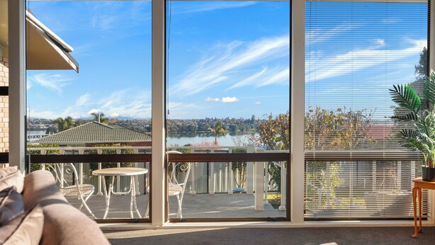 Un balcon offrant une vue sur un lac et sur le paysage urbain, aménagé avec un canapé, des fauteuils et une table.
