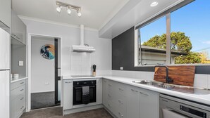 A modern kitchen with white cabinetry, a built-in oven, a dishwasher, and a window providing a view of the outdoors.