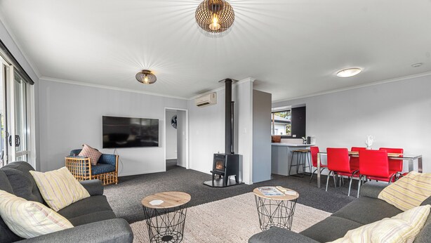 A modern living room with grey sofas, a TV, a fireplace, and a dining area with red chairs.