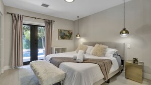 A modern bedroom with a large bed, a bench, a side table, and a view of the outdoors.