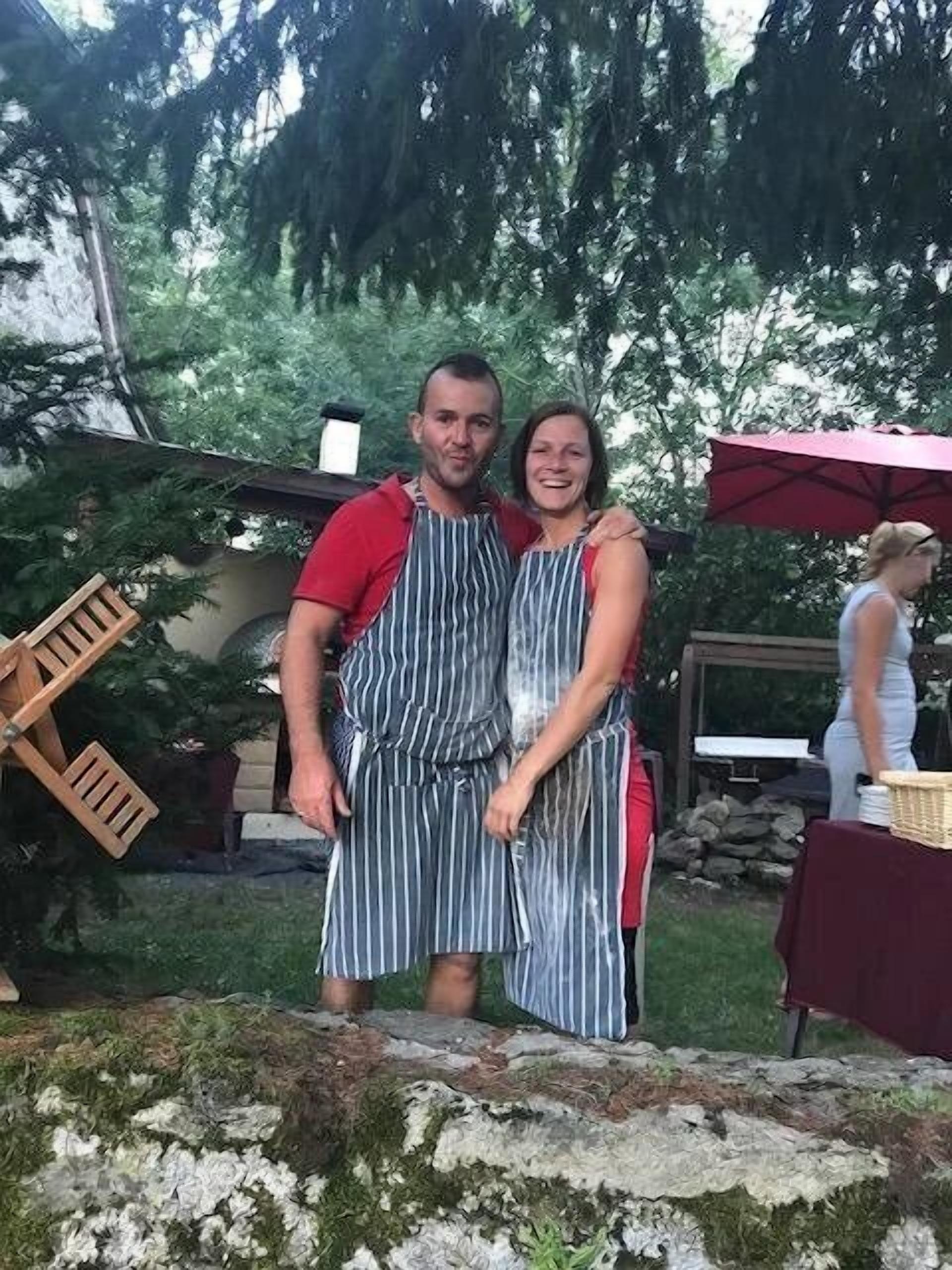 Un uomo e una donna in piedi all'aperto, entrambi con grembiuli a righe.