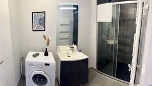 A modern bathroom with a Bosch washing machine, a vanity with a mirror, and a glass shower enclosure.