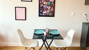 En matplats med ett bord dukat för två personer, två vita stolar, ett inramat konstverk ovanför bordet och ett eluttag på väggen.