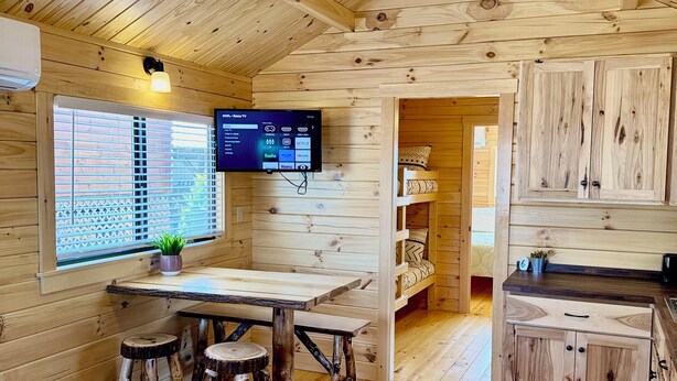 Ein Holzblockhaus im Inneren mit Essbereich, Küche und einem an der Wand montierten Fernseher.