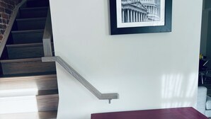 A staircase with wooden steps and a handrail, a framed picture of a building on the wall, and a dark wooden table with a round white cushion.