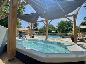 Un bain à remous sous une pergola en bois, avec une piscine en arrière-plan.