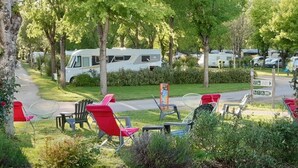 Un terrain de camping équipé d’emplacements pour camping-cars, d’un espace extérieur avec des sièges et d’un panneau indiquant les commodités disponibles.