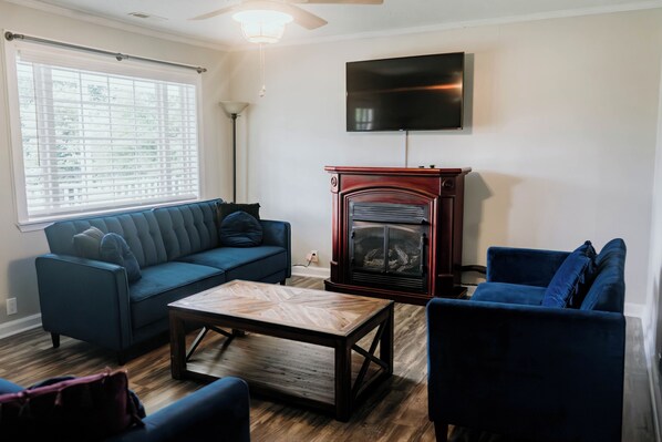 A living room with a blue sofa, a wooden coffee table, a fireplace, and a television mounted on the wall. - Beautiful Country House! (Kings Mountain)