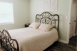 A neatly made bed with a metal headboard, a bedside table, and a window with blinds. - Beautiful Country House! (Kings Mountain)