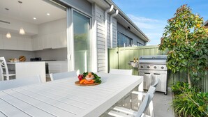 A modern kitchen with white cabinets, a large window, and a grill outside.