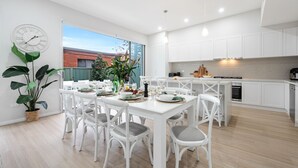Une cuisine moderne avec des meubles blancs, un coin repas avec des chaises blanches et une grande fenêtre donnant sur un jardin.