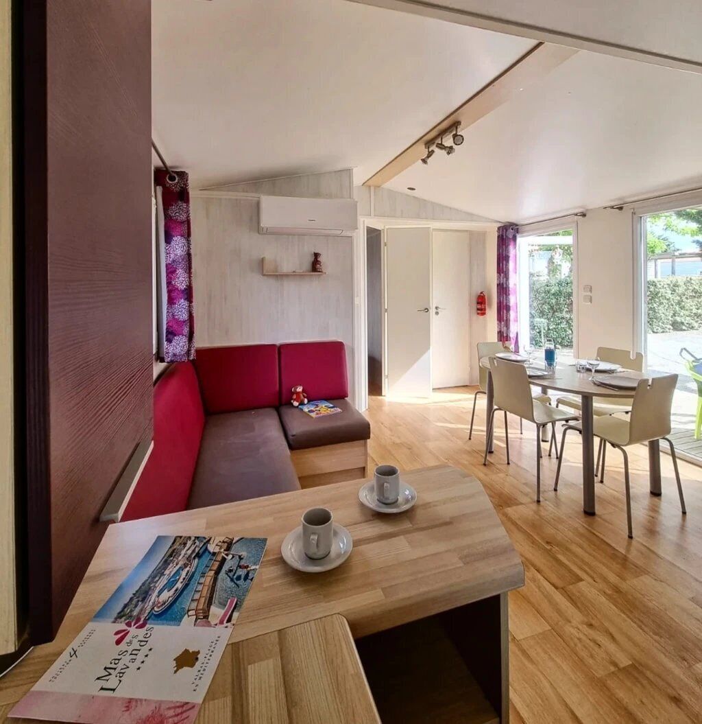 Uma sala de estar moderna com um sofá vermelho, uma mesa de centro de madeira com uma revista, e um espaço de jantar com uma mesa e cadeiras.