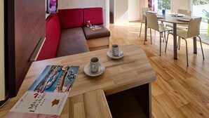 Una sala moderna con un sofá rojo, una mesa de centro de madera con una revista, y un comedor con mesa y sillas.