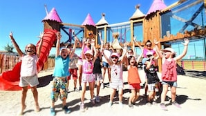 Eine Gruppe Kinder spielt auf einem Spielplatz mit Rutschen und Klettergeräten.