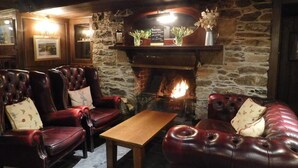 Un rincón de descanso acogedor con sofás y sillones de cuero, una mesa de centro de madera y una chimenea de piedra con fuego encendido.