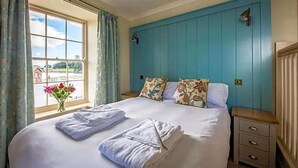 Un dormitorio con una cama grande, almohadas estampadas, una mesita de noche y un ventanal con cortinas.