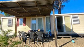 Un área de estar al aire libre techada con mesa y sillas, una terraza de madera y un edificio con ventanas y persianas.
