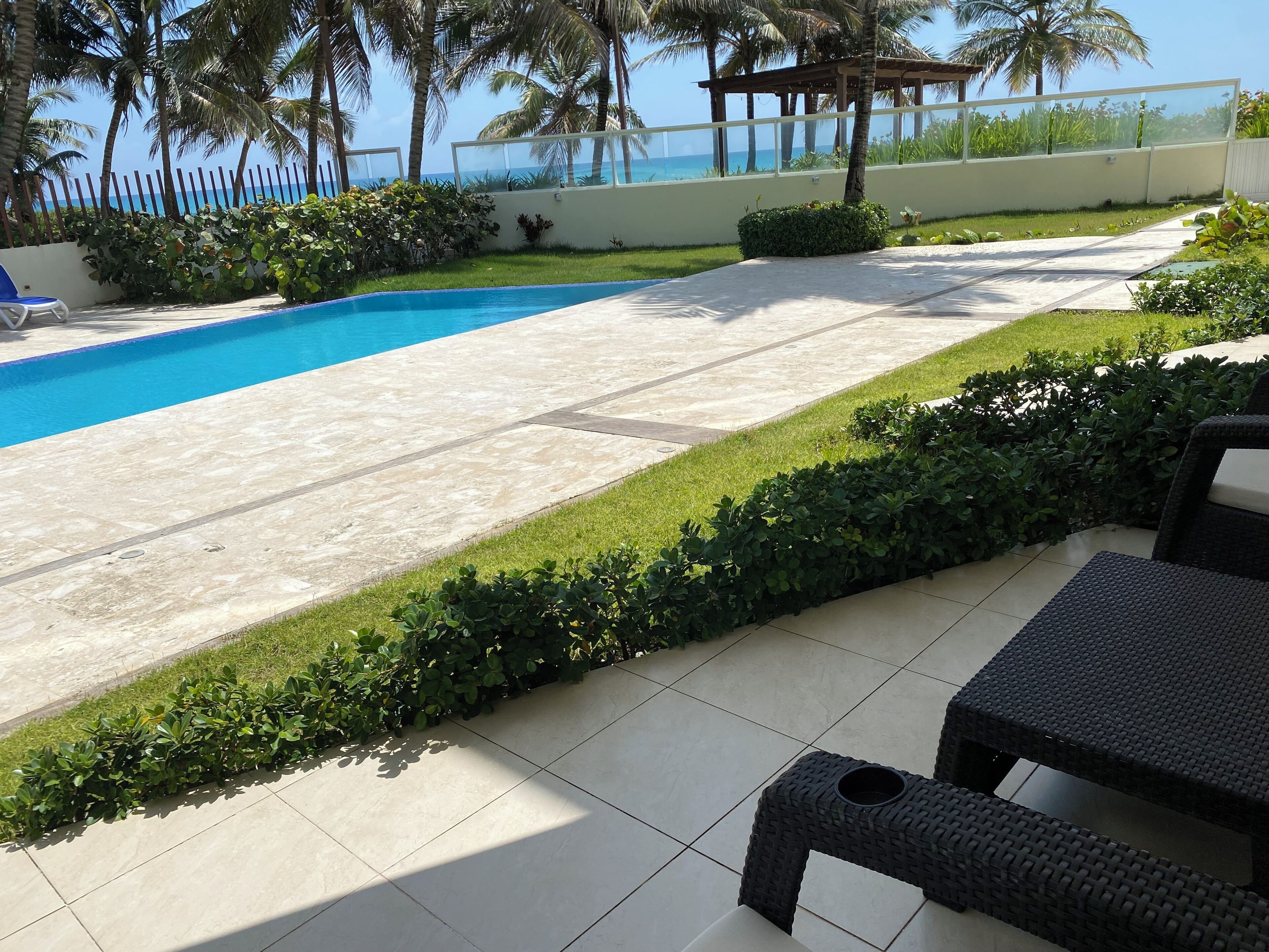 Un espace piscine offrant une vue dégagée sur l’océan, entouré de palmiers et agrémenté d’une pergola.