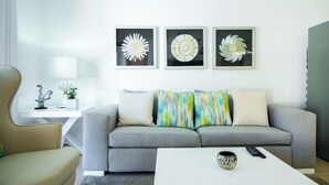Una sala de estar moderna con un sofá gris, una mesa de centro blanca y una lámpara. En la pared, hay tres obras de arte florales enmarcadas.